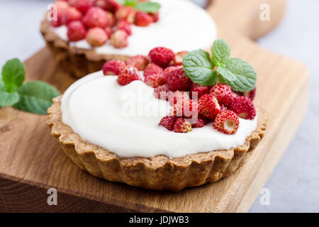 Tartelettes aux fraises sauvages avec la crème, de délicieux fruits d'été mini tartelettes sur planche à découper rustique Banque D'Images