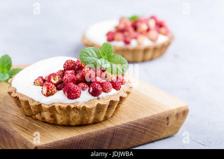 Tartelettes aux fraises sauvages avec la crème, de délicieux fruits d'été mini tartelettes sur planche à découper rustique Banque D'Images