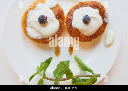 Deux crêpes au fromage cottage caillé sur plaque blanche avec des raisins secs, de la menthe et de baies de cassis sourire. Banque D'Images