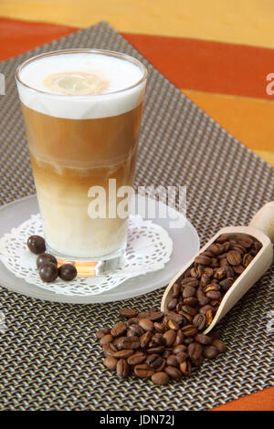 Latte Macchiato en verre avec des grains de café sur fond brun Banque D'Images