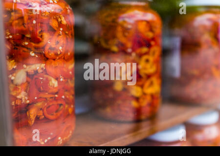 Les poivrons jaunes et rouges marinés dans de grands pots sur afficher derrière une vitre fenêtre avec pizza sign Banque D'Images