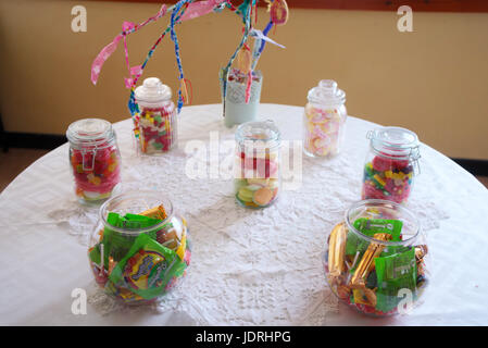 Les bocaux en verre remplis de bonbons à une table avec un tissu blanc Banque D'Images