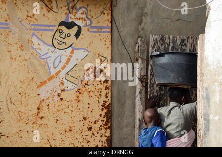 Dessin d'un cuisinier sur le mur rouillé. Femme Sénégalaise est porteur d'un seau en plastique sur la tête et a un enfant fixée à l'arrière. Yoff, Dakar, Sénégal Banque D'Images