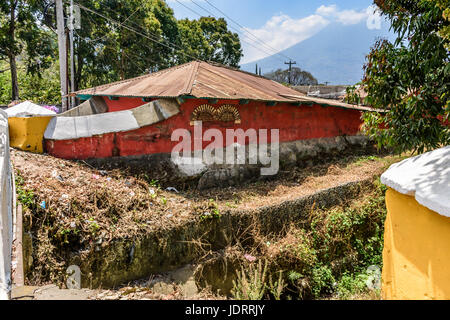 Antigua, Guatemala - mars 26, 2017 : mur rouge de la maison par la rivière à sec avec volcan agua derrière en ville coloniale et site du patrimoine mondial de l'UNESCO Banque D'Images