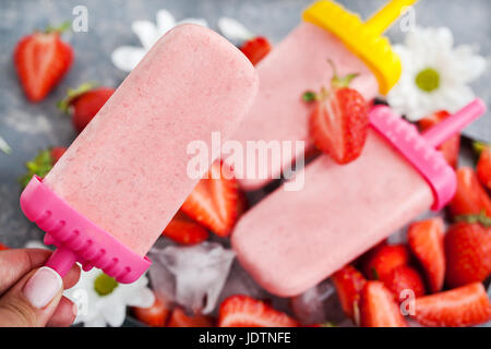 Sucettes glacées aux fraises délicieuse crème de glace avec de la glace et de baies fraîches autour, fond gris Banque D'Images