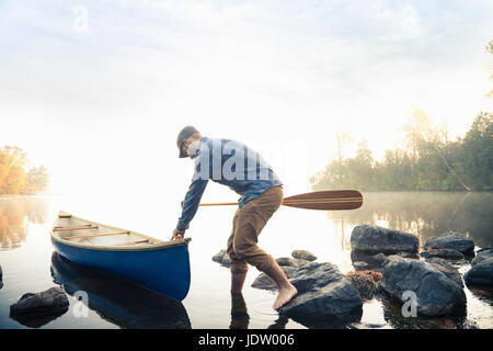 Man pushing canoe dans le lac encore Banque D'Images