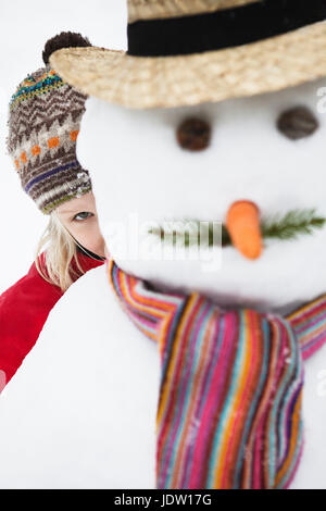 Girl peering out de derrière le Snowman Banque D'Images