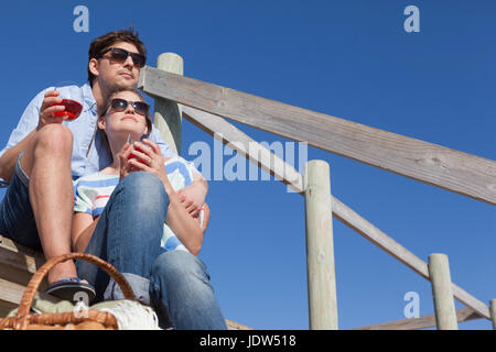 Couple sitting on boardwalk avec boissons, low angle Banque D'Images