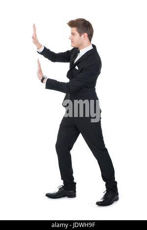 Vue latérale sur toute la longueur du mur invisible businessman pushing against white background Banque D'Images