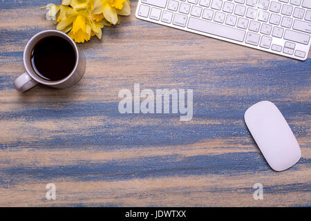 Travail de bureau avec clavier, bouquet de jonquilles, tasse de thé et la souris de l'ordinateur sur un fond de bois. Mise à plat, vue du dessus. Printemps fleurs jaunes. Banque D'Images