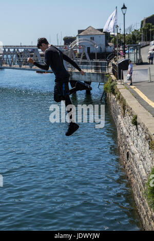 Un garçon saute dans l'eau au Barbican quais, port de Plymouth. Banque D'Images