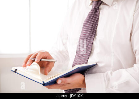 Businessman standing in office holding diary on white Banque D'Images