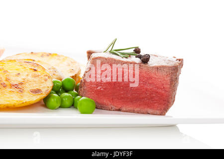 Mignon délicieux steak rare avec des pommes de terre et les pois sur plaque blanche, isolé sur fond blanc. La consommation de viande rouge culinaire. Banque D'Images