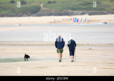 Un couple en train de marcher leur chien sur la plage à la baie de Daymer sur un jour nuageux en été à Cornwall, England, UK Banque D'Images