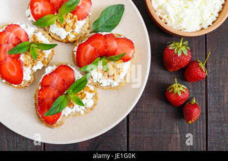 Mini sandwiches avec du fromage cottage, des fraises fraîches, décorées de feuilles de menthe sur le pain de seigle sur un fond de bois sombre. Une bonne nutrition. Healt Banque D'Images