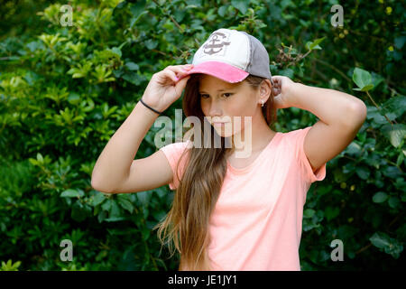 Jeune adolescente avec de longs cheveux blonds avec casquette de baseball. En plein air avec un fond vert. Banque D'Images