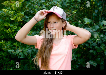 Jeune adolescente avec de longs cheveux blonds avec casquette de baseball. En plein air avec un fond vert. Banque D'Images