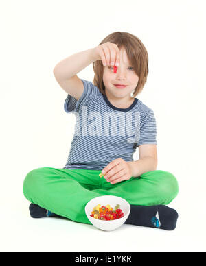 Un garçon avec les cheveux bruns eating gummy bears, arrière-plan blanc, isolé Banque D'Images