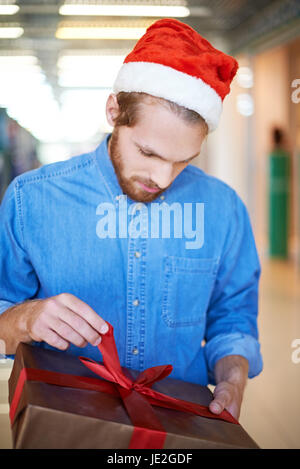 Guy à Santa cap déballage de cadeau de Noël Banque D'Images