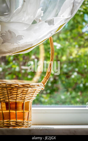 Panier en osier en bois debout sur un rebord de fenêtre sur une claire journée d'été Banque D'Images