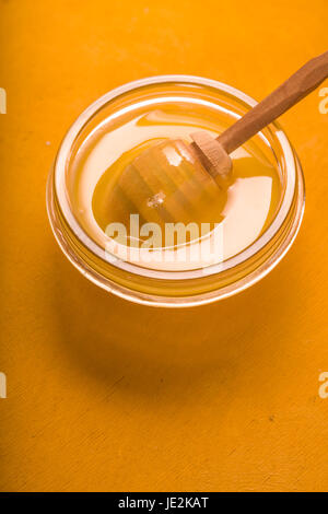 Le miel sur le bol en verre avec balancier sur le fond jaune à la verticale Banque D'Images