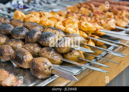 Pommes de terre appétissantes, des brochettes et shish kebab grillés sur les brochettes, libre à l'extérieur. L'alimentation de rue. Banque D'Images