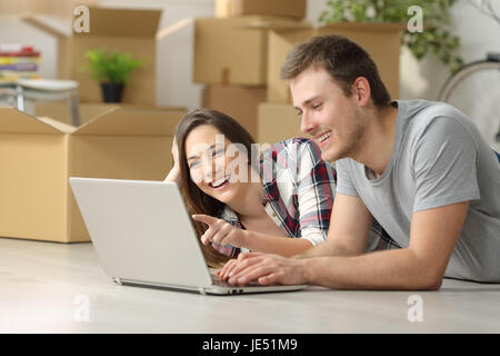 Happy casual couple déménagement recherche d'informations sur la ligne dans un pc se trouvant sur le plancher avec des boîtes à l'arrière-plan Banque D'Images