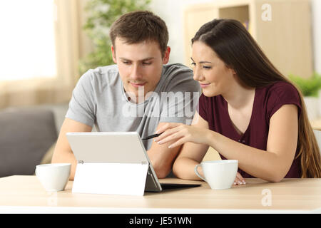 Couple recherche sur le contenu de la ligne avec un tablet pc assis dans une table dans la salle de séjour à la maison avec une fenêtre à l'arrière-plan Banque D'Images