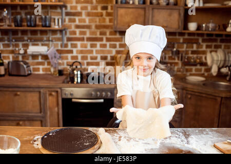 Petite fille faire de la pâte à pizza sur une table en bois dans la cuisine Banque D'Images