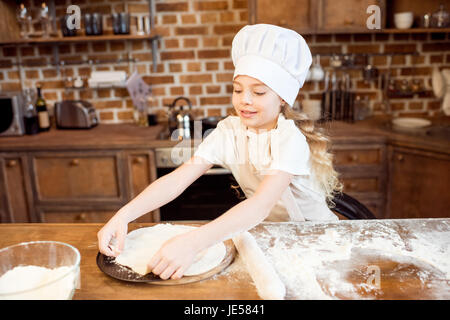 Petite fille faire de la pâte à pizza sur une table en bois dans la cuisine Banque D'Images