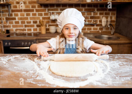 Girl en chef hat le déploiement de pâte à pizza crue Banque D'Images