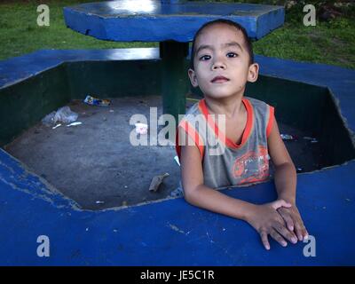 ANTIPOLO CITY, PHILIPPINES - le 13 juin 2017 : un jeune garçon frappe une pose devant l'appareil photo tout en étant assis sur un banc de parc. Banque D'Images