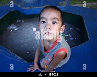 ANTIPOLO CITY, PHILIPPINES - le 13 juin 2017 : un jeune garçon frappe une pose devant l'appareil photo tout en étant assis sur un banc de parc. Banque D'Images