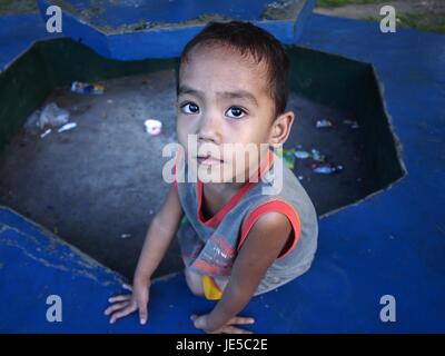 ANTIPOLO CITY, PHILIPPINES - le 13 juin 2017 : un jeune garçon frappe une pose devant l'appareil photo tout en étant assis sur un banc de parc. Banque D'Images