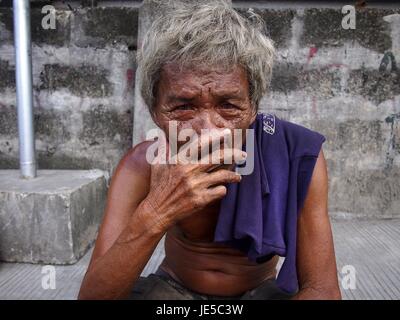 ANTIPOLO CITY, PHILIPPINES - le 14 juin 2017 : Un vieil homme avec des cheveux gris et la peau ridée pose devant l'appareil photo alors qu'il repose sur un trottoir. Banque D'Images