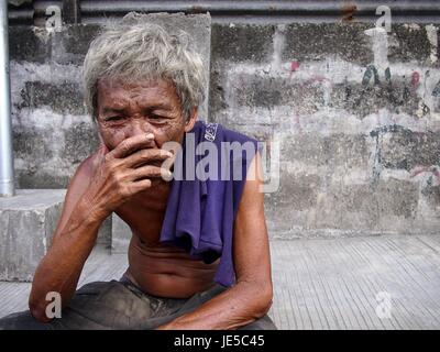 ANTIPOLO CITY, PHILIPPINES - le 14 juin 2017 : Un vieil homme avec des cheveux gris et la peau ridée pose devant l'appareil photo alors qu'il repose sur un trottoir. Banque D'Images