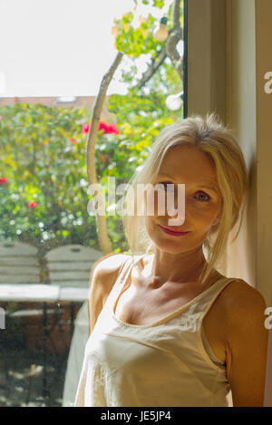 Mature Woman leaning against window, portrait Banque D'Images