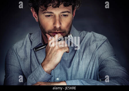 Homme tenant un stylet, regardant vers le bas en pensée avec la main sous le menton Banque D'Images