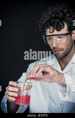Chemist pouring liquid from test tube dans le bécher Banque D'Images