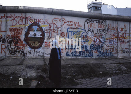 Une dame lit le graffiti sur le mur de Berlin, l'Allemagne de l'est tandis que les gardes frontière. Berlin 1987 Banque D'Images