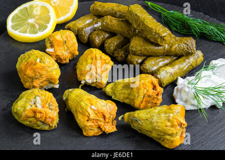 De délicieuses feuilles de vigne farcies et squash blossoms (le dolma traditionnels de la cuisine méditerranéenne) sur noir plat avec sauce tzatziki, tranche de citron Banque D'Images