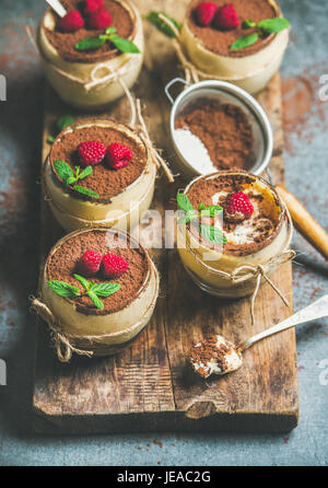Tiramisu dessert italien fait maison en verres individuels avec des feuilles de menthe, framboises mûres fraîches et de poudre de cacao sur planche de bois rustique gris plus con Banque D'Images