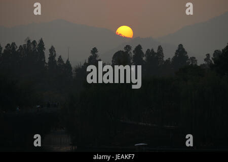Cette image capture un magnifique coucher de soleil sur le lac de l'Ouest (Xihu) à Hangzhou, en Chine. Connu pour sa beauté pittoresque, le lac est une destination touristique populaire, surtout au crépuscule lorsque le soleil couchant se reflète sur l'eau. Banque D'Images