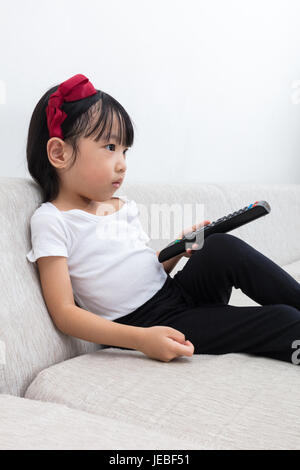 Chinois asiatique little girl holding a télécommande du téléviseur assis sur le canapé dans le salon à la maison. Banque D'Images