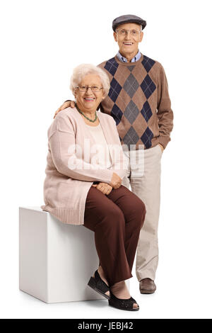 Femme mature assis sur un cube avec un homme mûr debout à côté d'elle isolé sur fond blanc Banque D'Images