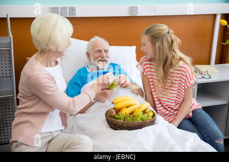 Grand-mère et petite-fille de fruits la visite à l'hôpital du patient. male patient in hospital bed concept Banque D'Images