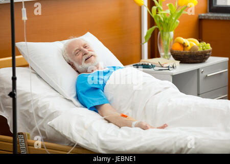 Smiling senior patient avec drop counter lying in hospital bed Banque D'Images