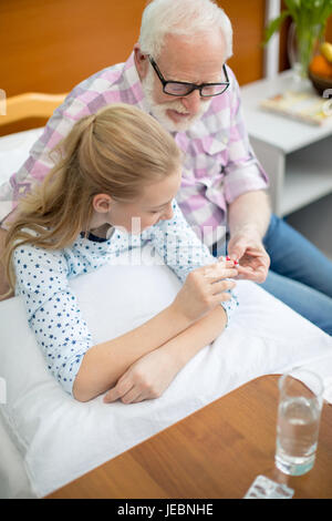 Grand-père dans les lunettes et petite-fille malade holding pills in hospital Banque D'Images