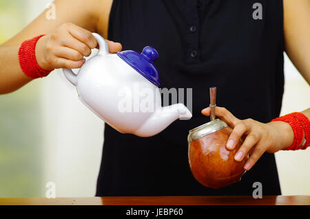 Woman holding white petit pot verser de l'eau chaude en tasse traditionnelle avec la paille qui le métal typique, la préparation de boisson populaire appelé mate. Banque D'Images