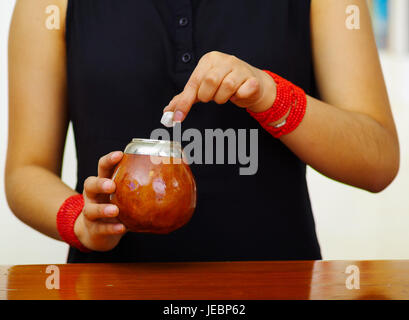 Woman holding mate traditionnelle tasse, addding cube de sucre à l'aide d'autre part, l'American Herbal loisirs boire. Banque D'Images